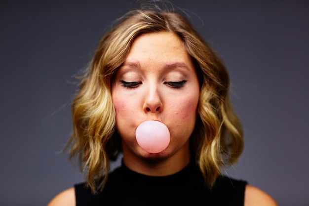 Foto close-up van een vrouw die kauwgom blaast op een grijze achtergrond