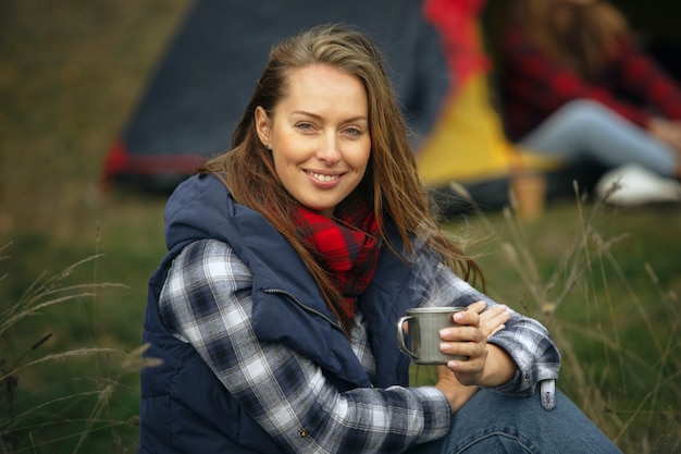 Close-up van een vrouw die lacht en thee drinkt met een groep vrienden op een achtergrond op de camping in het bos.