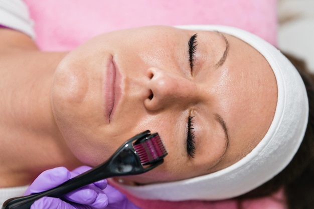 Close-up van een vrouw die ligt met een schoonheidsspecialiste die cosmetische rollen op haar gezicht gebruikt in een spa.