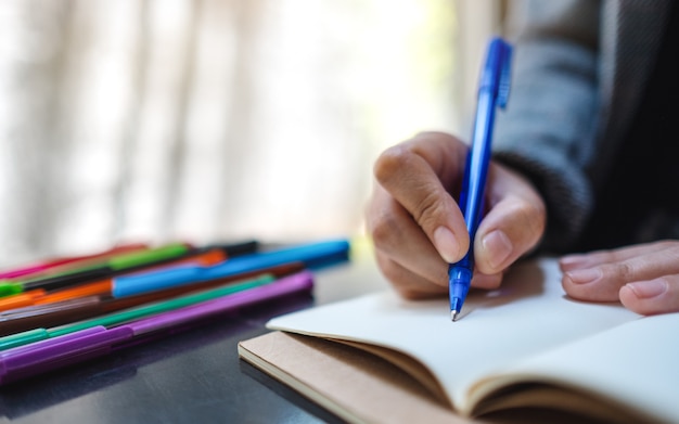 Close-up van een vrouw die op een leeg notitieboekje met gekleurde pennen op de lijst schrijft