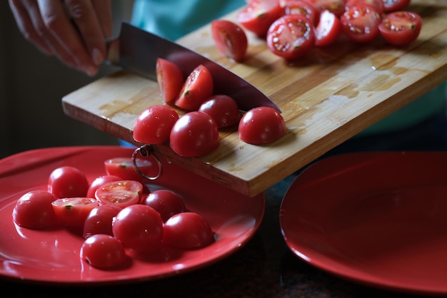 Foto close-up van een vrouw die tomaten op een houten bord snijdt en gesneden groenten op een bord legt