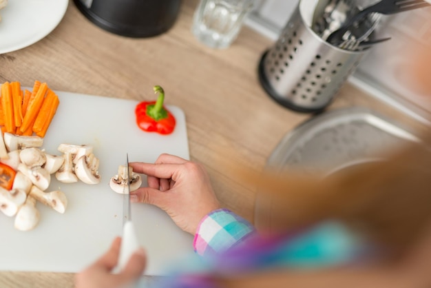 Close-up van een vrouw die vegetarisch voedsel snijdt op het keukenbord. Achteraanzicht.