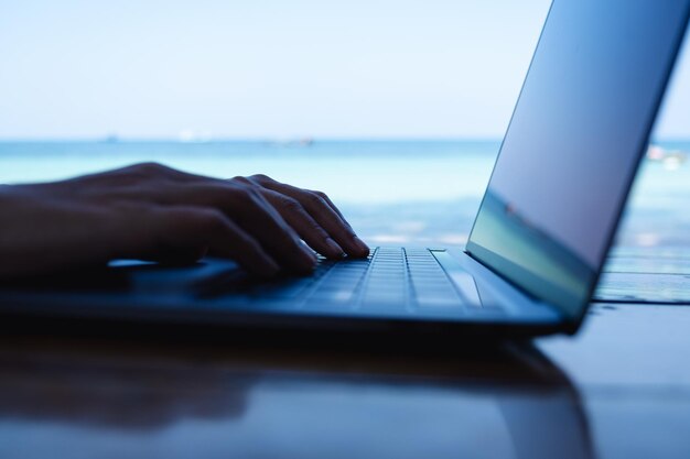 Foto close-up van een vrouw die werkt en typt op een laptopcomputer op het strand