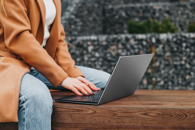 Close up van een vrouw handen typen in een laptop in de straat tegen een kantoorgebouw. Zakenvrouw werkafstand