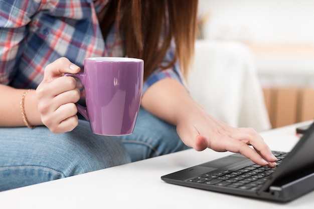 Close up van een vrouw handen typen in een laptop zittend op de Bank met kopje thee