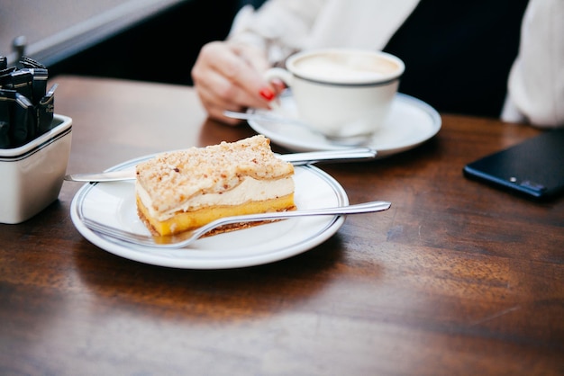 Close-up van een vrouw in een café met een kopje koffie in haar handen naast een cake en een telefoon