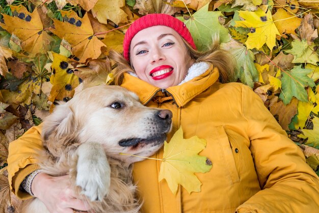 Close-up van een vrouw in een jas en een retrieverhond liggen tussen de gele herfstbladeren in het park.