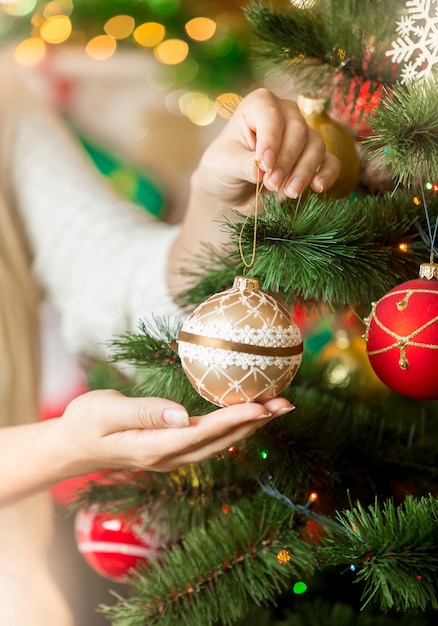 Close-up van een vrouw in een trui die de kerstboom versiert met kerstballen