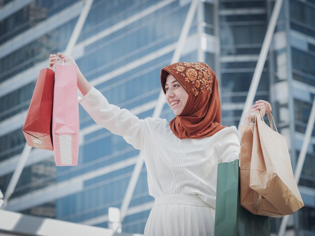 Foto close-up van een vrouw met een hijab die winkeltassen vasthoudt tegen een gebouw in de stad