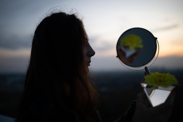 Close-up van een vrouw met een spiegel tegen de hemel tijdens zonsondergang