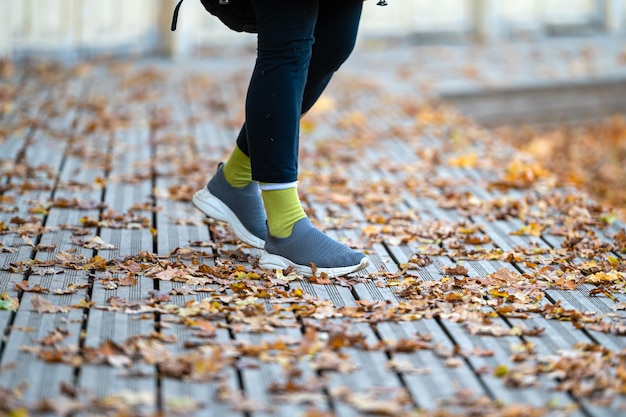 Close-up van een vrouwelijke benen op houten wandelpaden bedekt met herfstbladeren