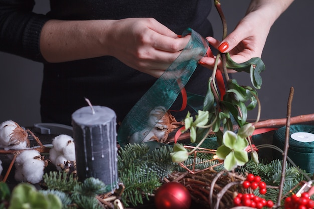 Close-up van een vrouwelijke bloemist die een Kerstmiskroon van spartakken, Kerstmisbellen en natuurlijk decor maakt