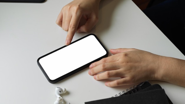 Close-up van een vrouwelijke hand met behulp van slimme telefoon met wit leeg leeg scherm op witte bureau tafel.