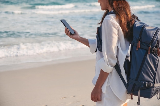 Close-up van een vrouwelijke reiziger die een mobiele telefoon aan zee vasthoudt en gebruikt