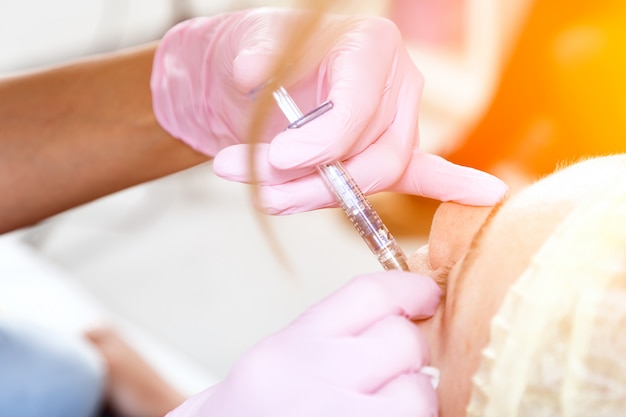 Close-up van een vrouwelijke schoonheidsspecialist die een injectie van Botox injecteert in de jukbeenderen van een jonge vrouw om de vorm te corrigeren