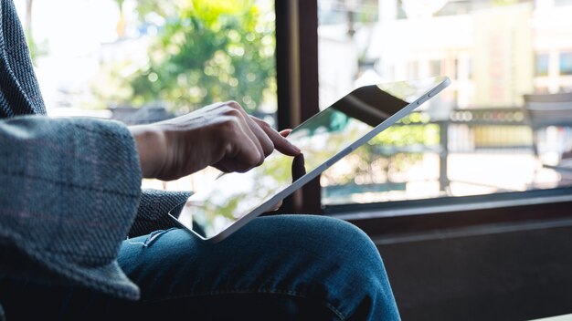 Foto close-up van een vrouwenholding en het richten van vinger op het scherm van tabletpc terwijl het zitten in koffie