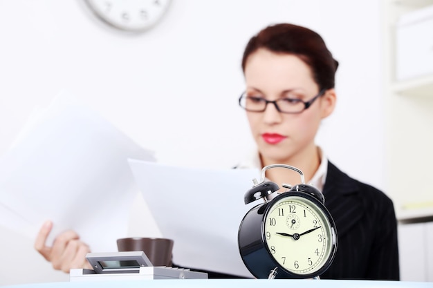 Foto close-up van een wekker met een vrouw die aan het bureau werkt