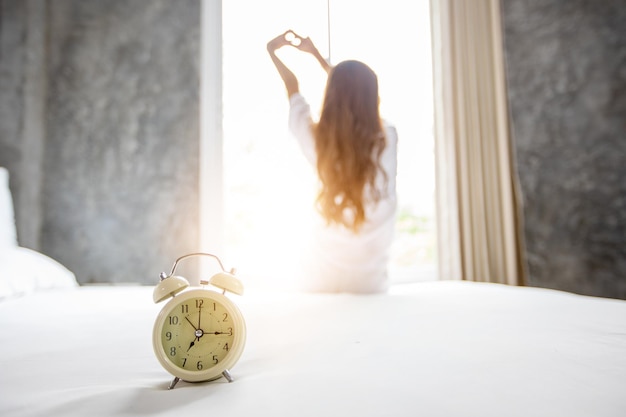 Foto close-up van een wekker op bed met een vrouw op de achtergrond