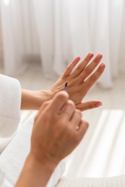 Foto close-up van een welgevormde vrouw die 's ochtends haar nagels lakt, zittend op het bed gekleed in een kamerjas.