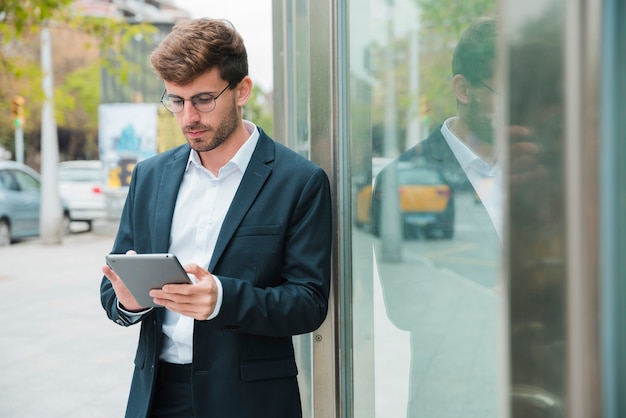 Close-up van een zakenman die dichtbij de glasdeur leunt die digitale tablet gebruikt