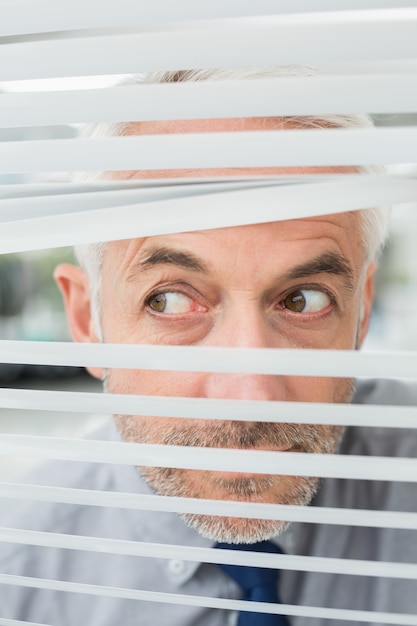 Foto close-up van een zakenman die door zonneblinden gluren