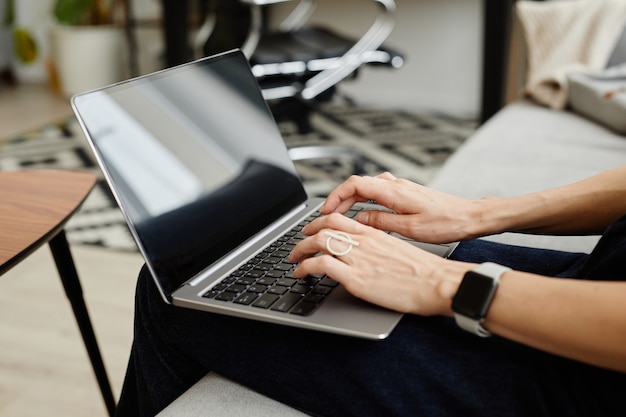 Close-up van een zakenvrouw die op de bank zit met een laptop op haar knieën en typt dat ze online werkt