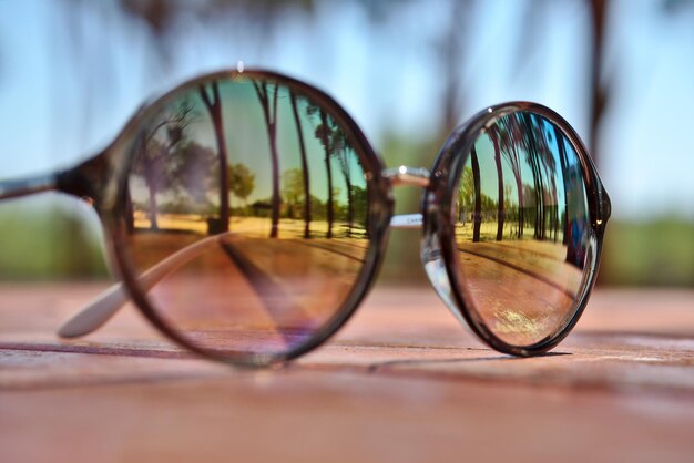 Foto close-up van een zonnebril met bomen die op de tafel reflecteren