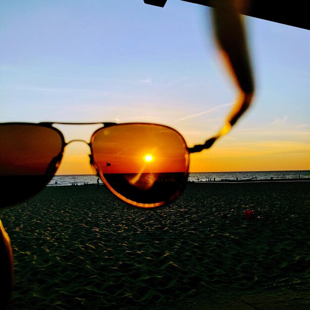 Close-up van een zonnebril op het strand tegen de hemel tijdens de zonsondergang