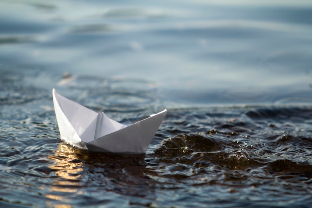 Close-up van eenvoudige kleine witte origamidocument boot die in blauw duidelijk rivier of zeewater onder heldere de zomerhemel drijft. Schoonheid van de natuur, vrijheid, dromen en fantasieën concept.