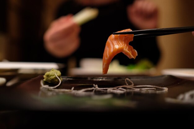 Close-up van eetstokjes met sashimi tegen een persoon die eten eet in een restaurant