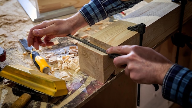 Close-up van ervaren timmerman in werkkleding en eigenaar van een klein bedrijf die in een houtbewerkingswerkplaats werkt met een beitel voor het uitsnijden van hout in de werkplaats op de tafel is een hamer en veel gereedschap