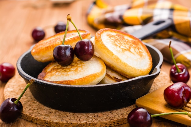 Close-up van gebakken pannenkoeken in een ijzeren pan en rijpe kersen op een houten tafel
