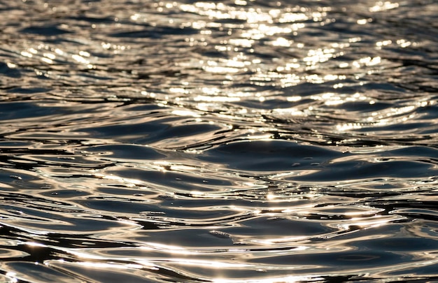 Foto close-up van gegolfd oppervlak van donker water met zonlicht bij gouden zonsondergang