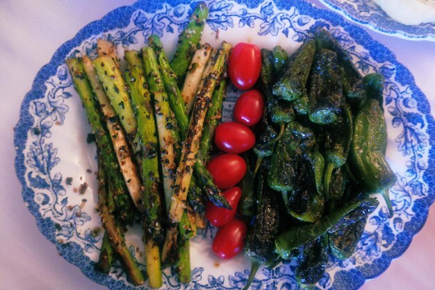 Foto close-up van gegrilde asperges met kersentomaten en groene chili peper op een bord
