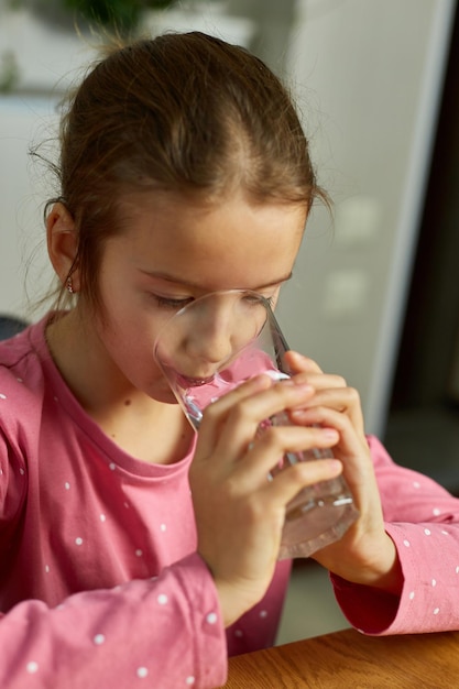 Close up van gelukkig klein meisje glas zoet water drinken in de keuken