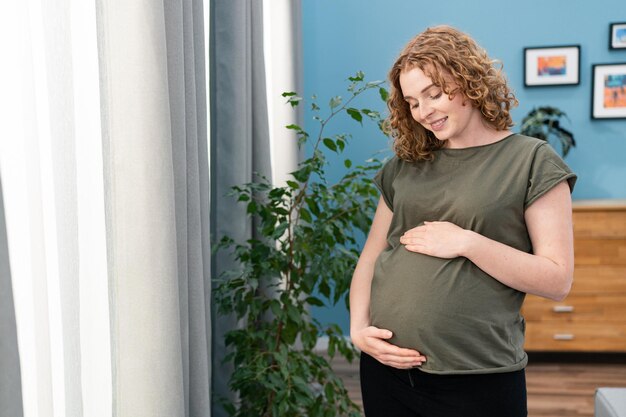 Close up van gelukkige zwangere vrouw met grote buik bij raam