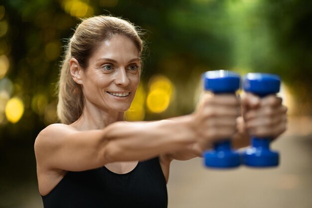 Close-up van gemotiveerde sportieve vrouw die met dumbbells in park traint