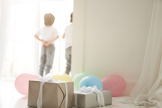 Close-up van geschenkdozen en kleurrijke ballonnen voorbereid voor het vieren van vakantie met twee nieuwsgierige Latijns-tweelingjongens, kinderen die op de achtergrond staan. Vakantie, cadeautjes, kinderconcept