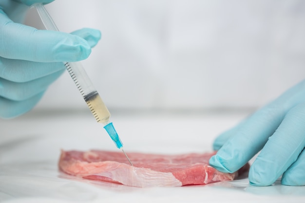 Close-up van gloved onderzoeker handen die vlees inspuiten