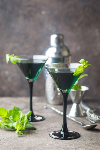 Close-up van groene cocktails in martini-glazen met muntblaadjes over grijs