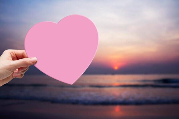 Foto close-up van hand die hartvorm vasthoudt op het strand tegen zee en lucht tijdens zonsondergang