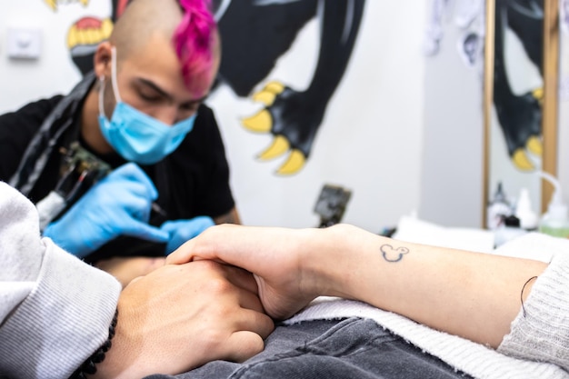 Close-up van handen die elkaar vasthouden terwijl ze een tatoeage krijgen in de tattoo-studio