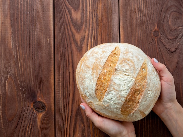 Close-up van handen met een rond heel brood van tarwebrood Bruine houten achtergrond Bovenaanzicht plat lag Bakkerijconcept Kopieer ruimte