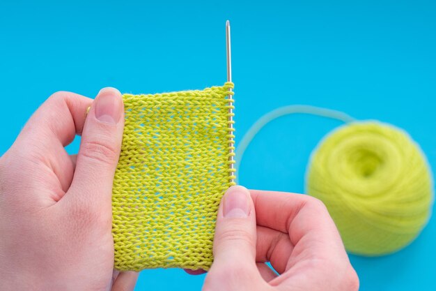 Close-up van handen van blanke vrouw breien met groene draad op een blauwe achtergrond klaar patroon kopie ruimte