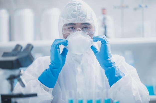 Close-up van handen van een jonge onherkenbare wetenschapper, onderzoeker en arts die blauwe handhandschoenen draagt met witte PPE-kit en uniform met covid-19 gezichtsbeschermingsmasker voor veiligheid in laboratorium