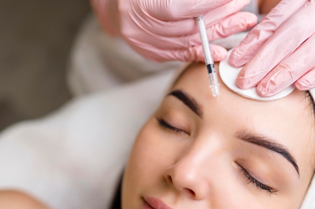 Close up van handen van jonge schoonheidsspecialist die botox injecteert in vrouwelijk gezicht Ze staat en glimlacht De vrouw is haar ogen gesloten met ontspanning