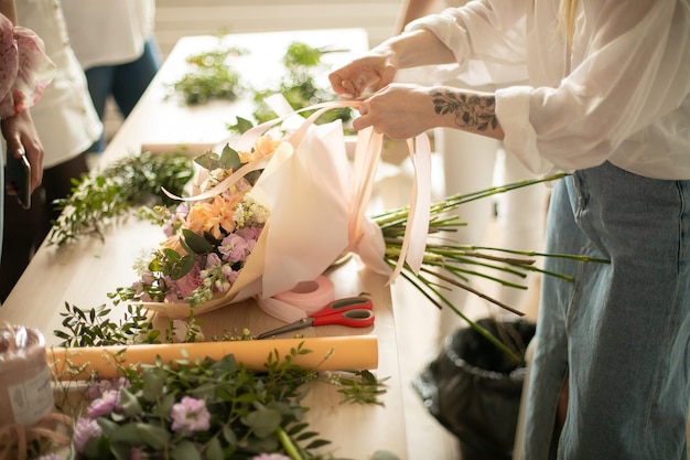 Close-up van handen van jonge vrouwenbloemist die boeket van bloemen met lint maakt