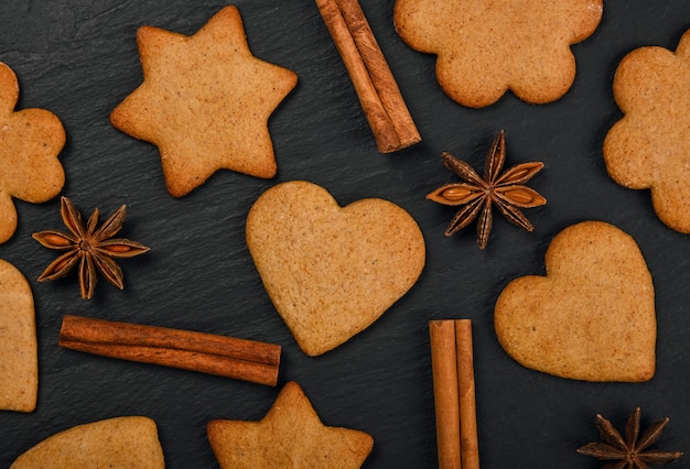 Close-up van hart en stervormige peperkoek kerstkoekjes met kaneel en steranijs kruiden op zwarte leisteen achtergrond, verhoogde bovenaanzicht, direct erboven