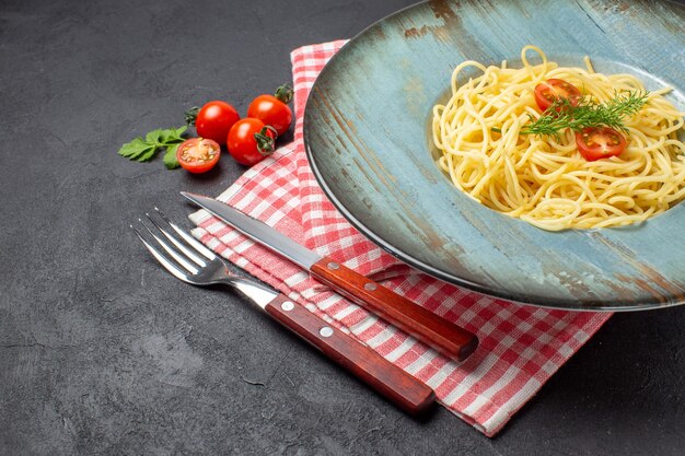 Close-up van heerlijke spagetti geserveerd met tomatengroen en bestek op een rode gestripte handdoek op zwarte achtergrond