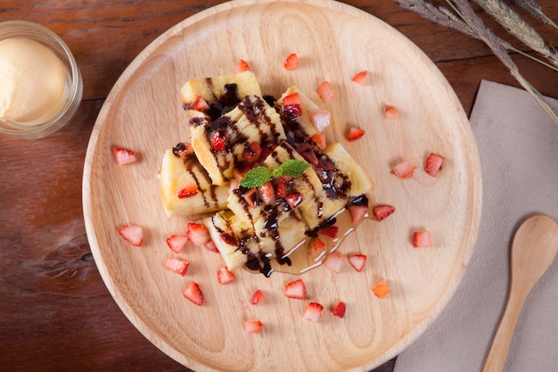 Close-up van het dessert dat brood, aardbeienbessen, caramel en pepermuntblad bovenop op houten plaat en op de houten tafel heeft